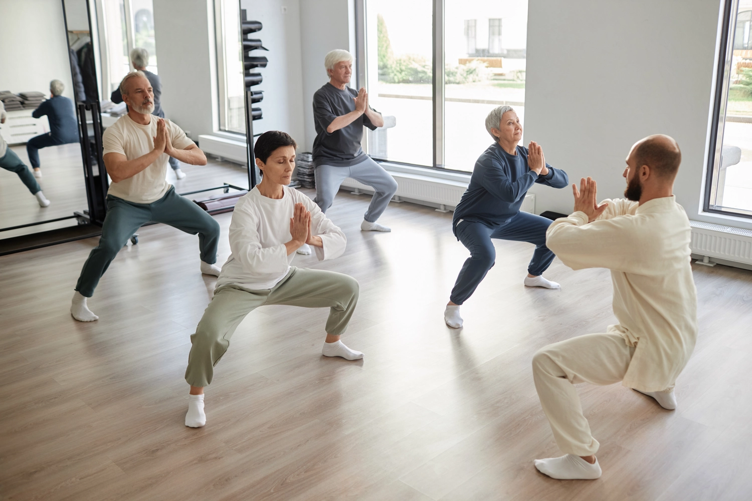 Chan tao - Institut für Gesundheit - Seitenansicht älterer Menschen im Fitnessstudio, Fokus auf bärtiger älterer Mann, der sich während des Qigong-Unterrichts im Fitnessstudio als Bogenschütze beim Schießen ausgibt