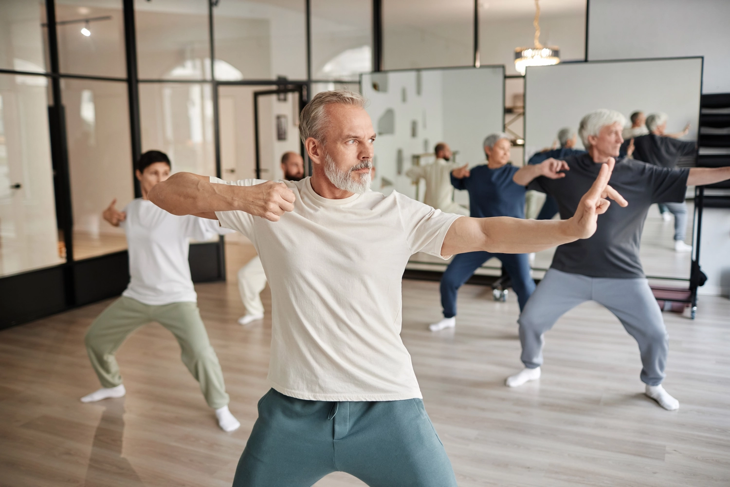 Chan tao - Institut für Gesundheit - Seitenansicht älterer Menschen im Fitnessstudio, Fokus auf bärtiger älterer Mann, der sich während des Qigong-Unterrichts im Fitnessstudio als Bogenschütze beim Schießen ausgibt
